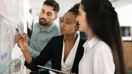 man and two women at a chalkboard in the office